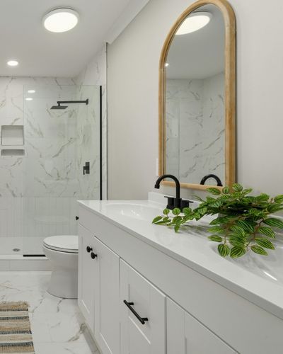 A bathroom with white flooring, granite countertops and shower, and white cabinets