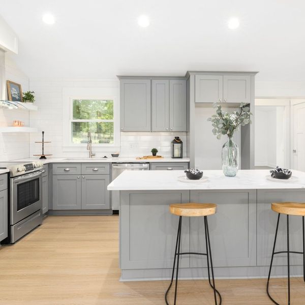 A newly remodeled kitchen with grey cabinets, wood floors, and white countertops. There is a kitchen island in the middle of the room