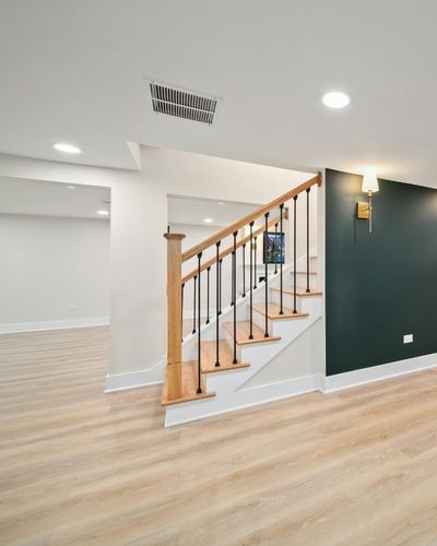 A finished basement with an open floor plan, a wide stair case with a wood railing, and an accent wall