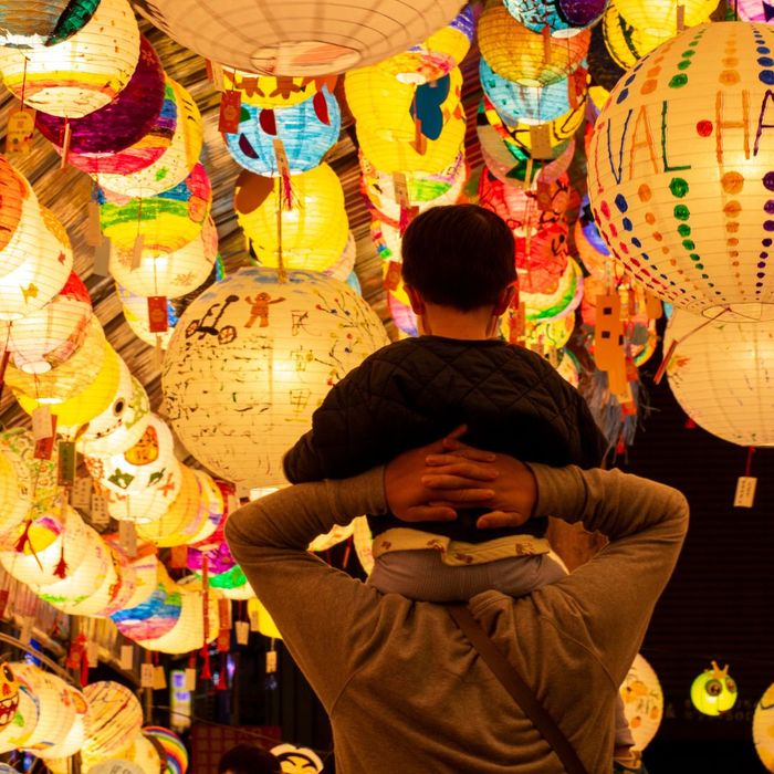 child sitting on shoulders of adult walking under colorful lanterns