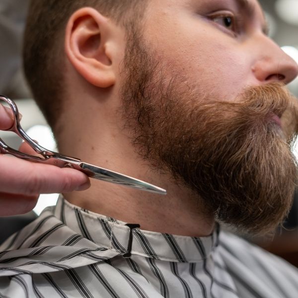 a close up of a man's beard with a barber holding scissors next to him