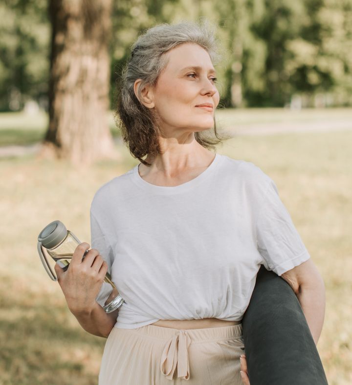 Middle aged woman walking through a park holding a water bottle while thinking about the qualities of Hyaluronic Acid Dermal Filler Products
