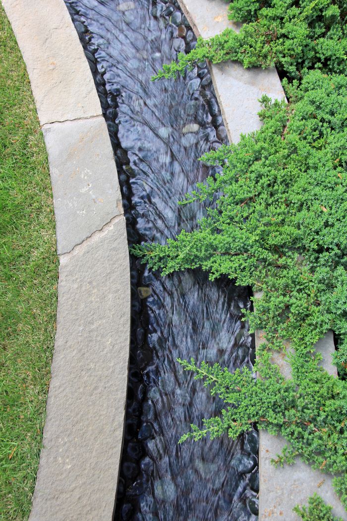 Close-up of textured limestone serpentine fountain with flowing water outside John Staub home in River Oaks.