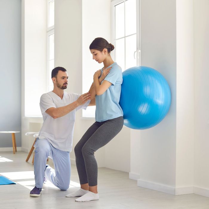 Chiropractor helping a woman use an exercise ball to help back pain. 