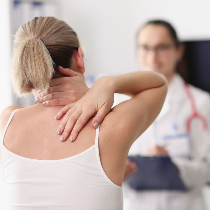 Woman speaking with a chiropractor while reaching behind her to hold her neck and back. 