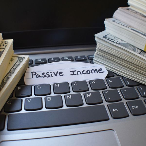 Stacks of money on a keyboard and a piece of paper that says "passive income"