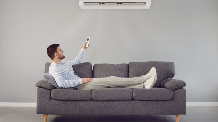 person on couch adjusting ac with remote
