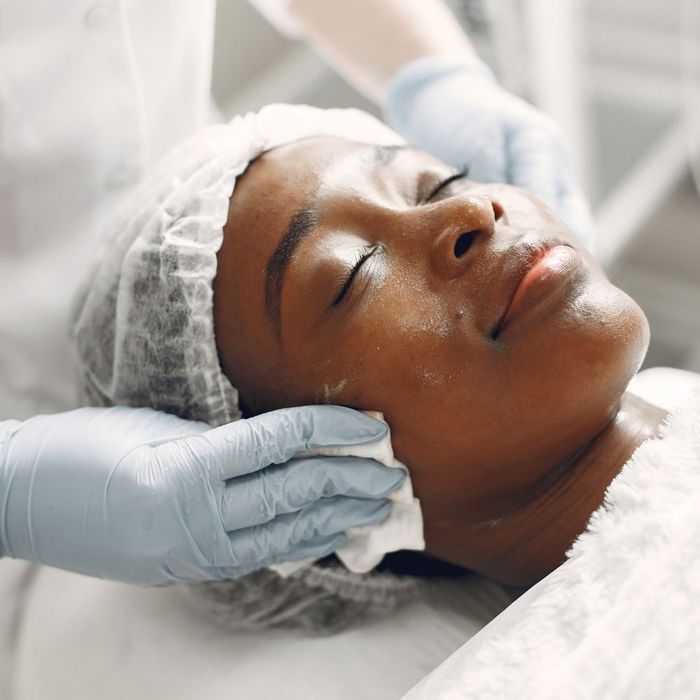 An aesthetician performing a relaxing facial treatment on a woman with her hair wrapped in a white towel.