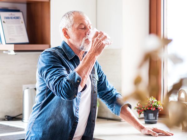 Older man drinking glass of water in his kitchen