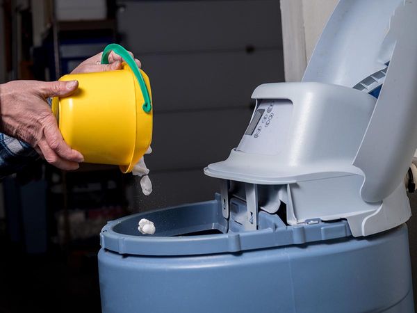 Man adding salt pellets to the reservoir of a water softener