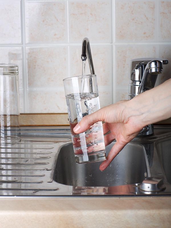 Person filling up a glass of water with the kitchen faucet
