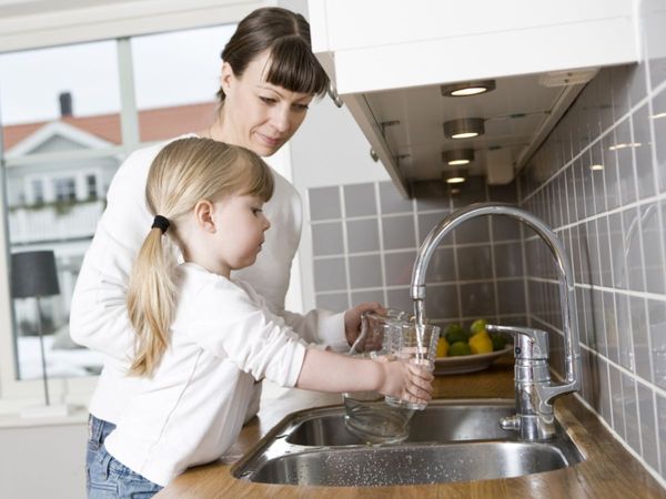woman helps little girl fill a water pitcher in the sink