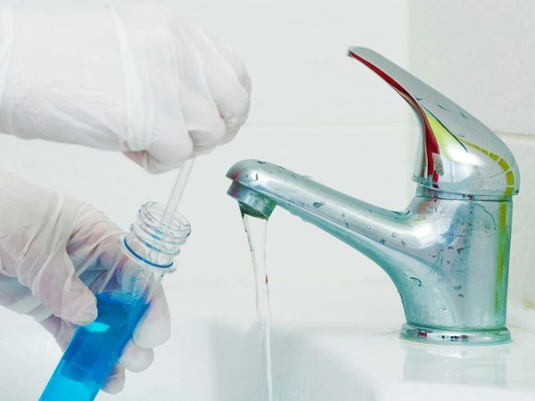Person wearing gloves and taking a water sample from a sink faucet
