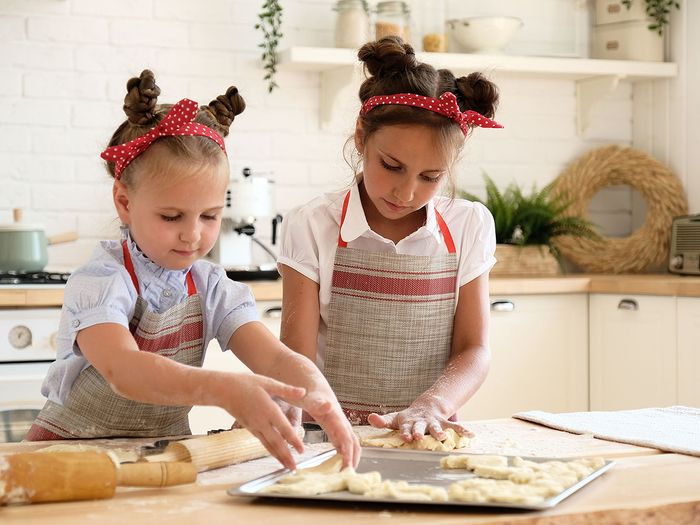 Two little girls prepping cookie dough on baking sheet