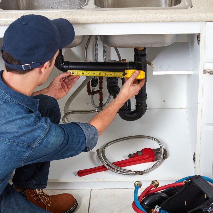 Plumber measuring a pipe under a sink