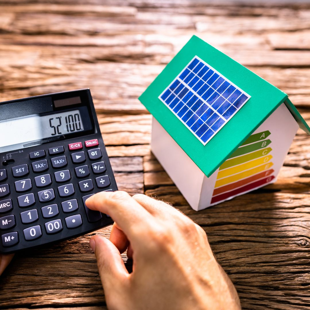 Small model home with solar panel on it, with person making calculations on calculator