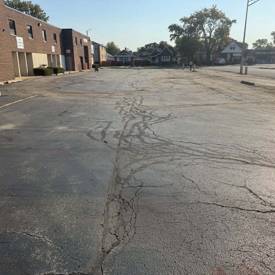 Old, cracked asphalt parking lot in front of an industrial building.