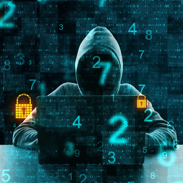 Hooded, unidentified person sitting at a laptop typing, with holographic numbers floating on the screen.