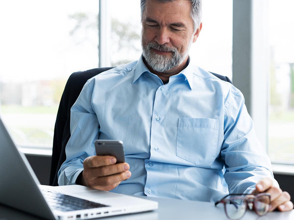 An image of a man sitting at a desk and looking at his phone.