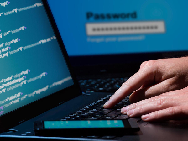Person using laptop displaying code next to a desktop displaying a password
