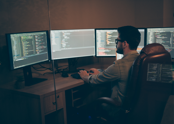 An image of a man working on code on four computers.