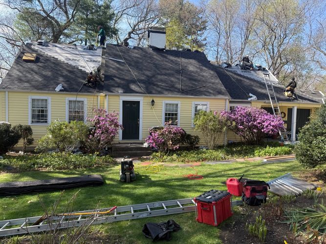 Professional roofing crew carefully laying down architectural asphalt shingles on a steep roof replacement job in Wellesley MA