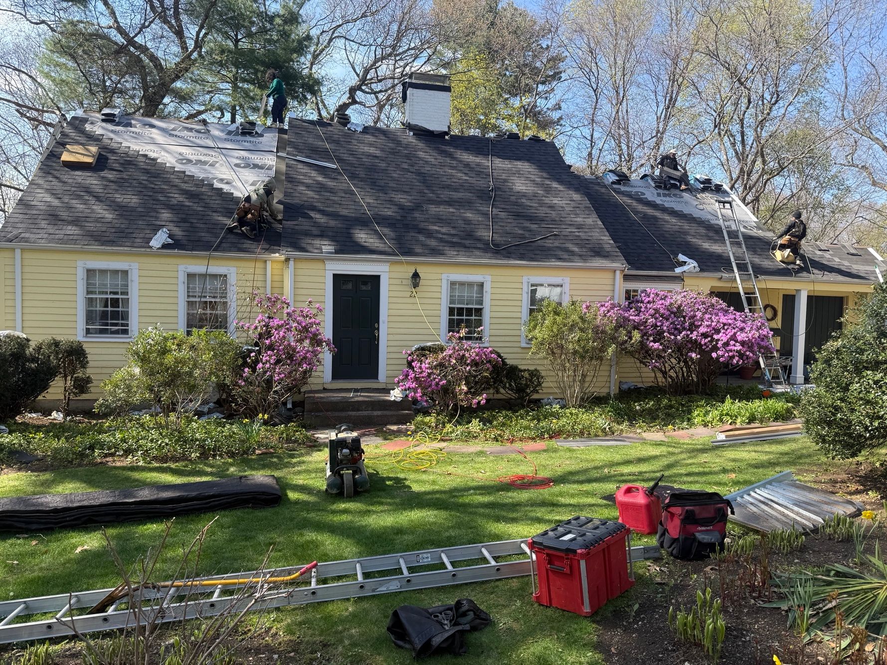 Professional roofing crew carefully laying down architectural asphalt shingles on a steep roof replacement job in Wellesley MA