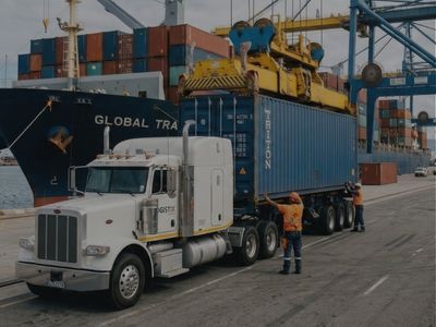 A semi-truck being loaded with a shipping container from a large ship A semi-truck being loaded with a shipping container from a large ship