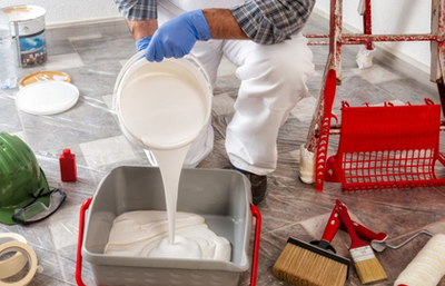 House painter in white overalls pour paint into container.