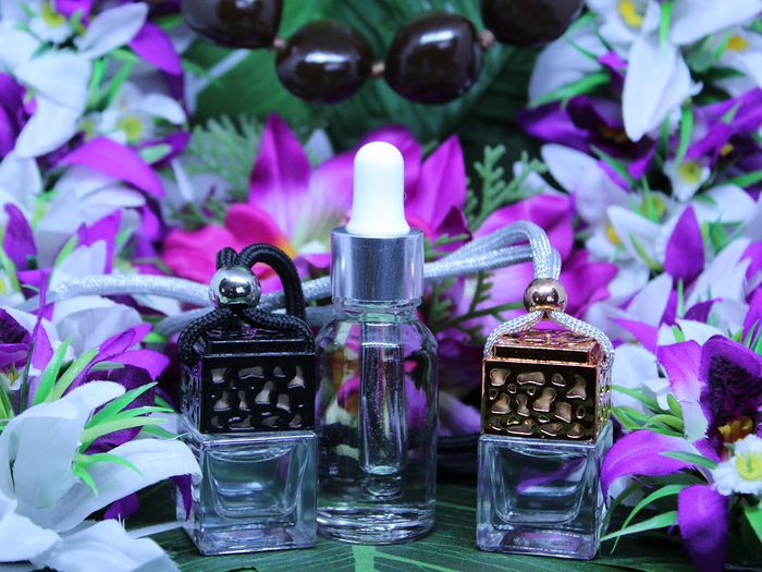 Three cases of scented, diffusible oils set before a gorgeous backdrop of purple and white Hawaiian flowers. 