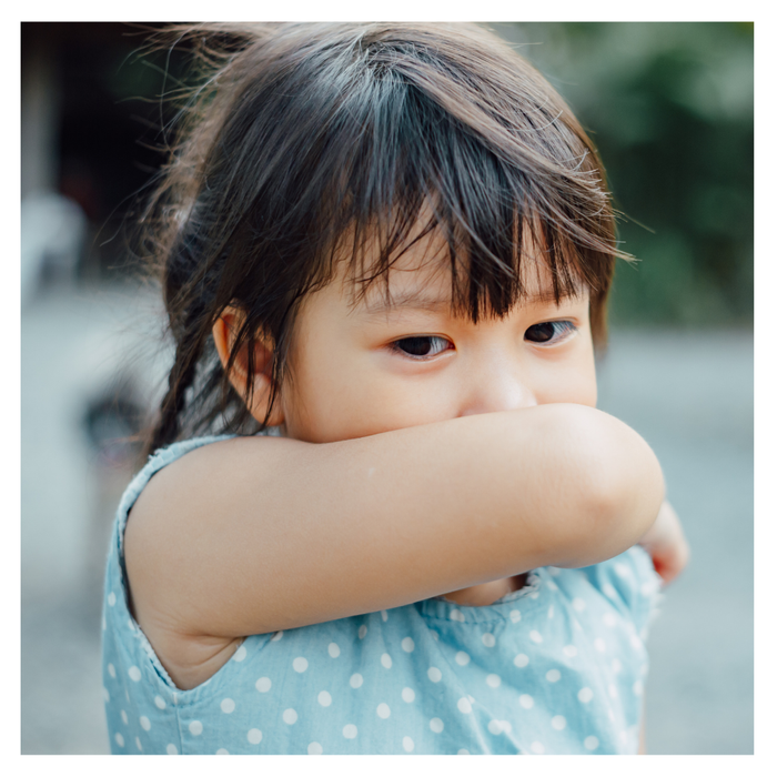 A little girl coughing into her arm