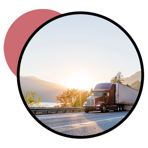 An image of a semi truck driving alongside a lake surrounded by mountains.