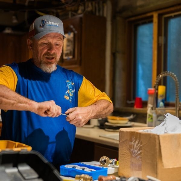 Experienced plumber installing or repairing a kitchen sink faucet fixture.