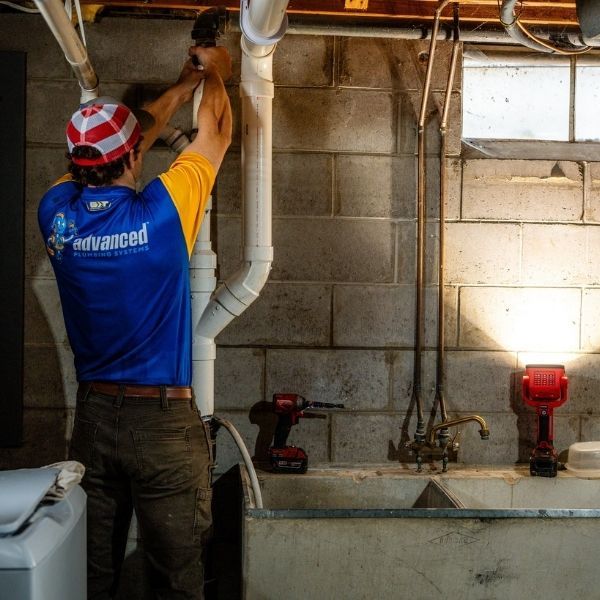 Licensed plumber inspecting and repairing pipes in a basement utility area.
