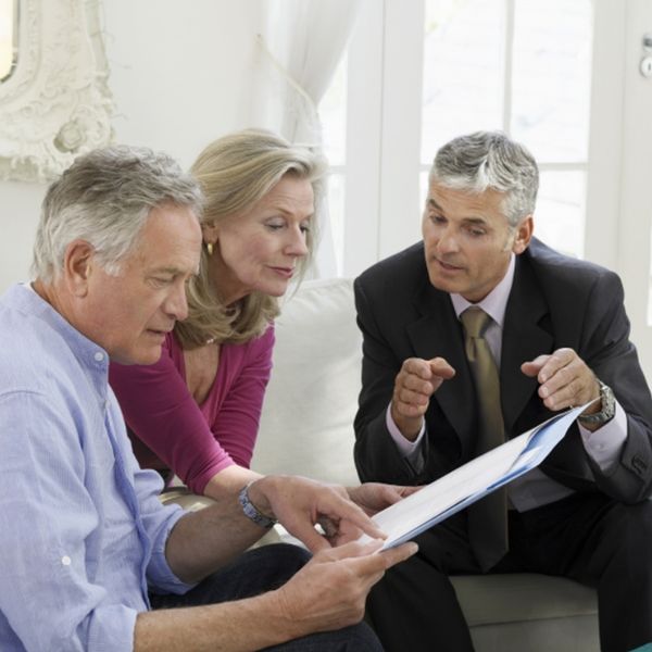 Three people discussing something, with one man pointing to a piece of paper in a file. 