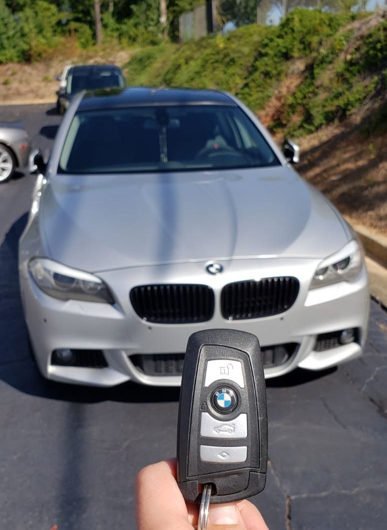 Hand holding a BMW key fob with a silver BMW in the background