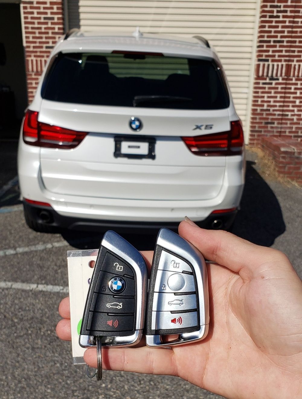 A hand holding two BMW key fobs with a white BMW in the background