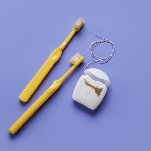 Two toothbrushes and some floss up against a purple background. 
