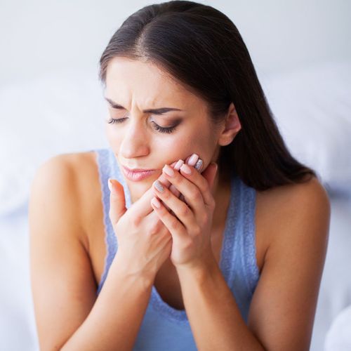 A woman sitting on her bed holding her mouth in pain