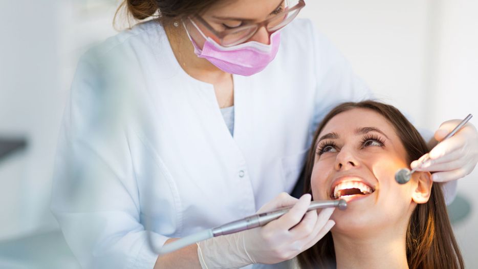 Dentist looking down at a smiling woman while putting tools near her mouth. 