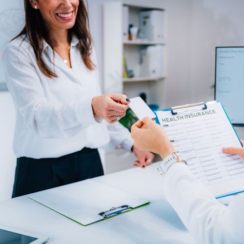A woman handing her dental insurance card to a receptionist at a dental office