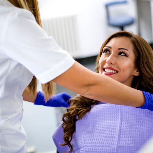 Dental hygienist putting a purple bib on a smiling woman.