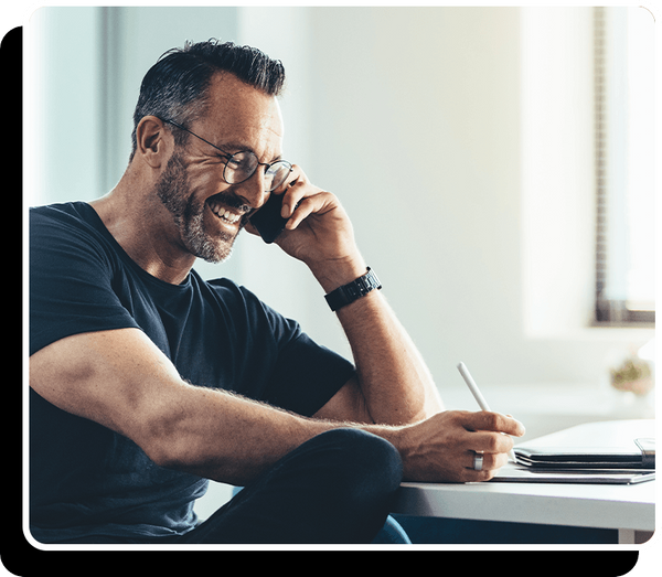 Man smiling and taking notes during phone call