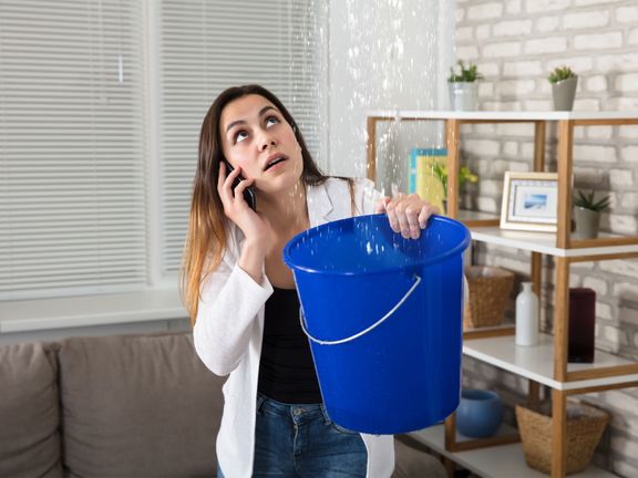 Woman on the phone while holding bucket to catch water drips