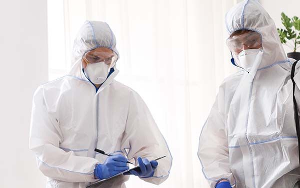 Two individuals in hazmat suits, one is writing on a clip board