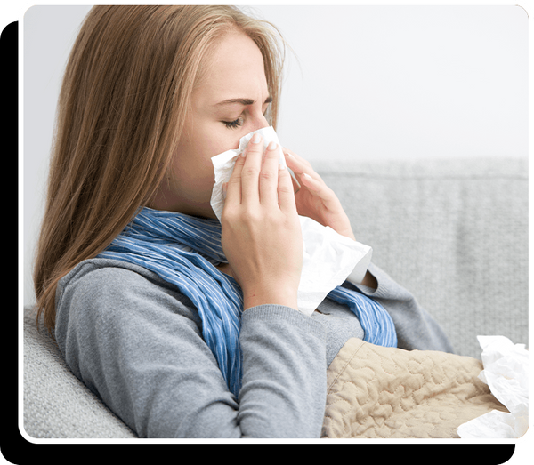 Woman blowing her nose while lying on a couch with a blanket