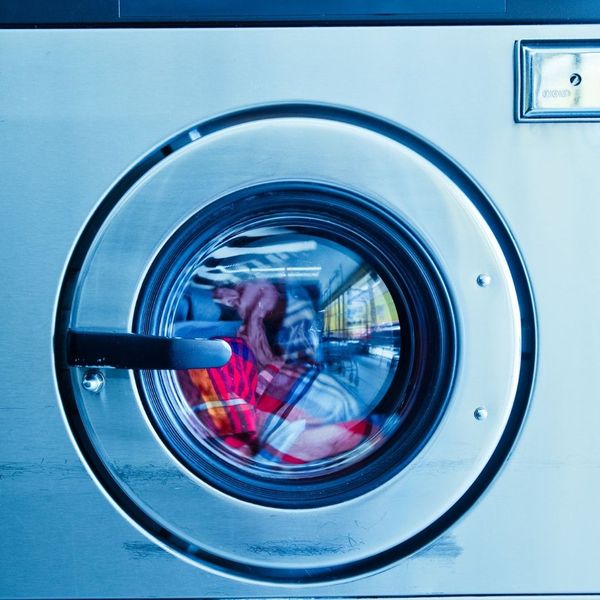 A close-up view of the glass door of a commercial washer, showing clothes spinning inside during a cycle.
