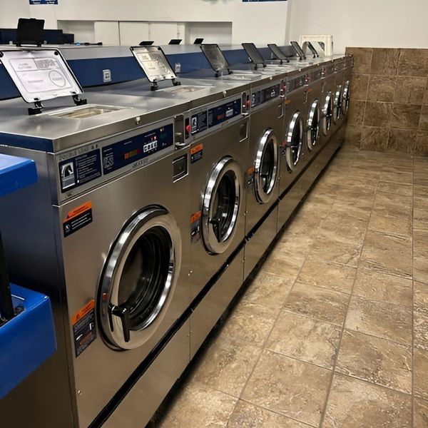A row of modern, stainless steel washing machines with open doors in a clean laundromat.