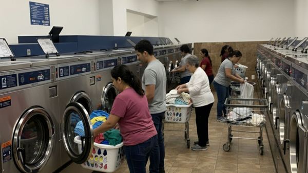 Customers actively load and unload laundry from stainless steel washing machines in a busy laundromat.