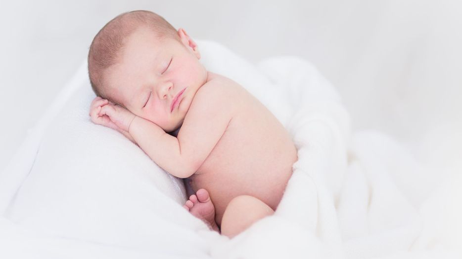 Newborn baby wrapped in a white blanket, posed for a photo. 